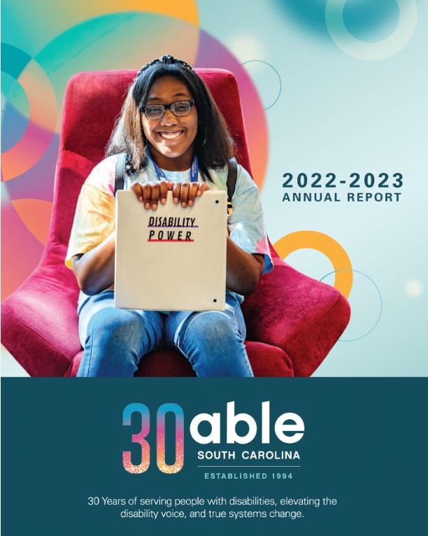 Able SC 2022-23 Annual Report cover image- Young African-American girl sitting in a red velvet chair, smiling and holding a notebook that says 'Disability Power' on the cover