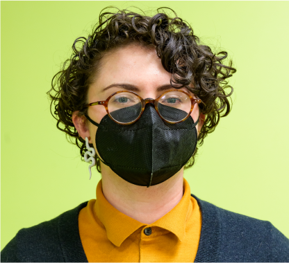 Photo of e.k. a white person with disabilities with curly brunette hair and glasses wearing a mask.