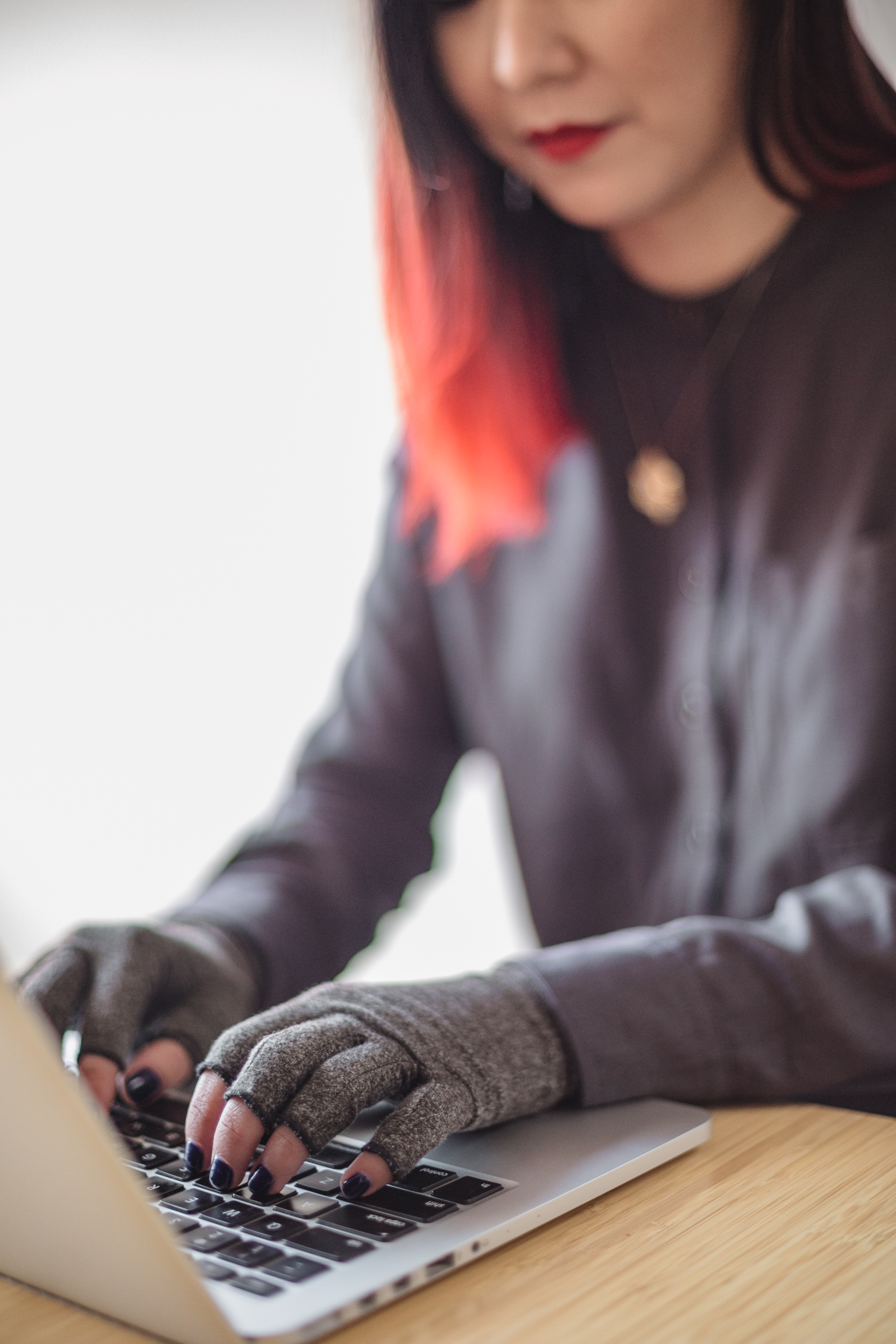 Nonbinary Asian person typing on a laptop while wearing compression gloves.