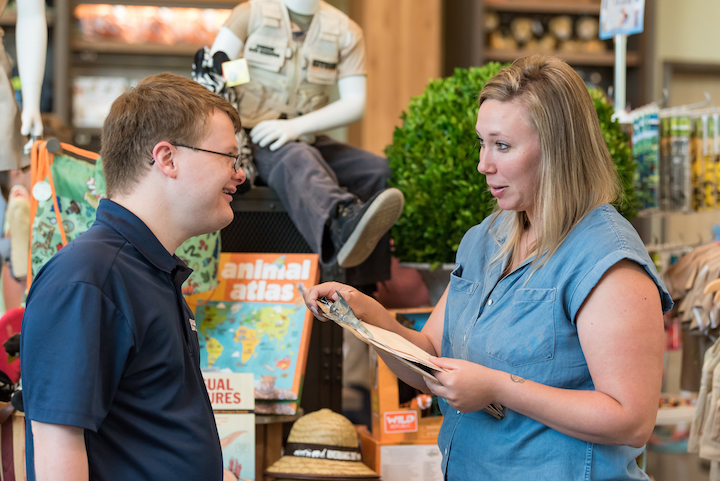 Photo of a woman holding a clipboard while talking to an employee at the Riverbanks Zoo gift shop.