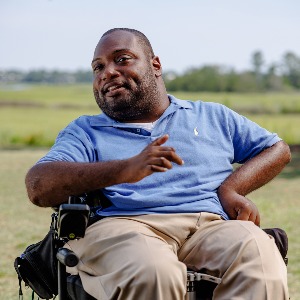 A Black man in a power wheelchair speaking outside.