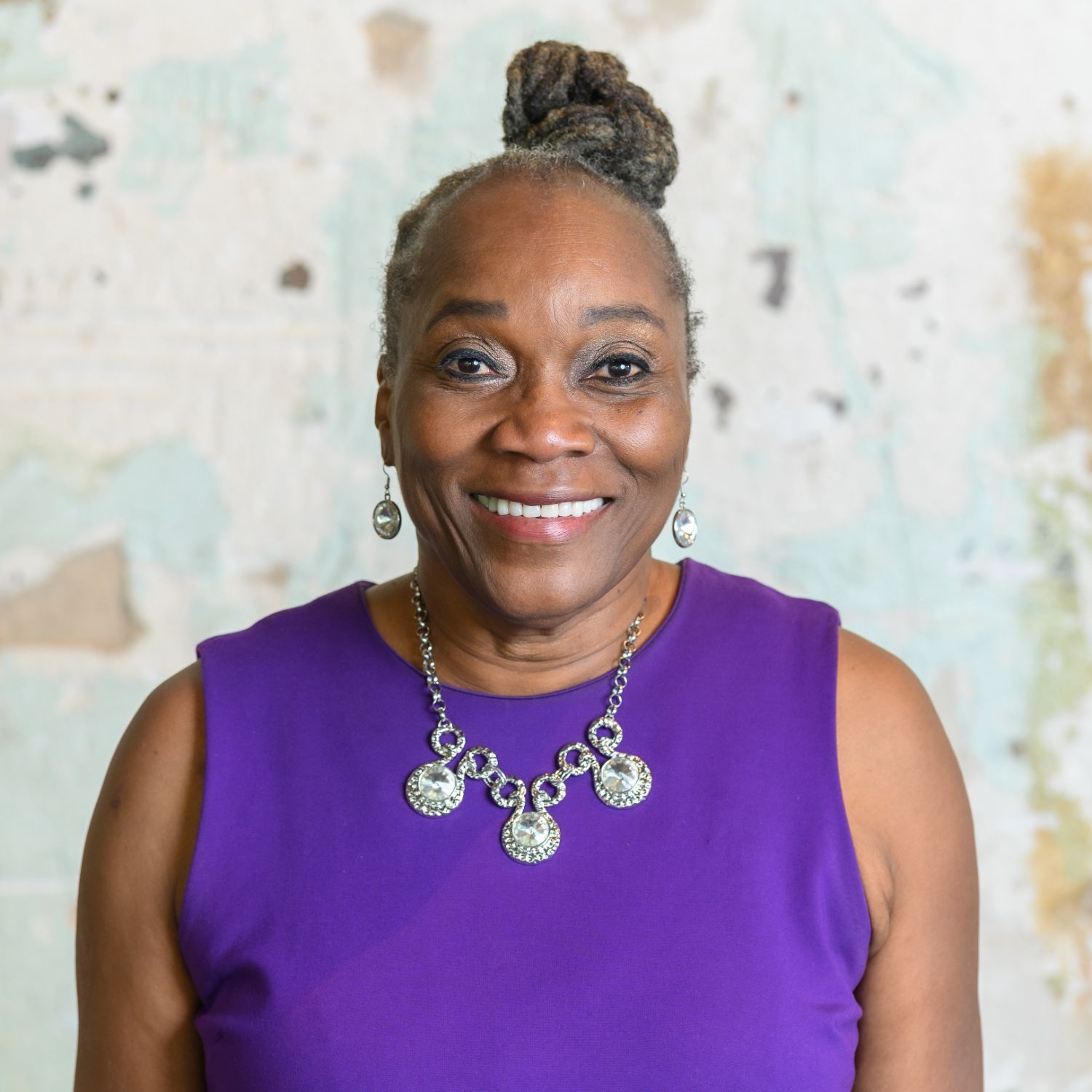 Photo of Vertelle, a senior Black woman with graying hair in an updo wearing a purple dress.