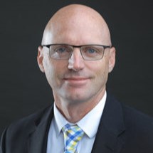 Photo of Tyler, a white man with no hair wearing glasses and a suit.