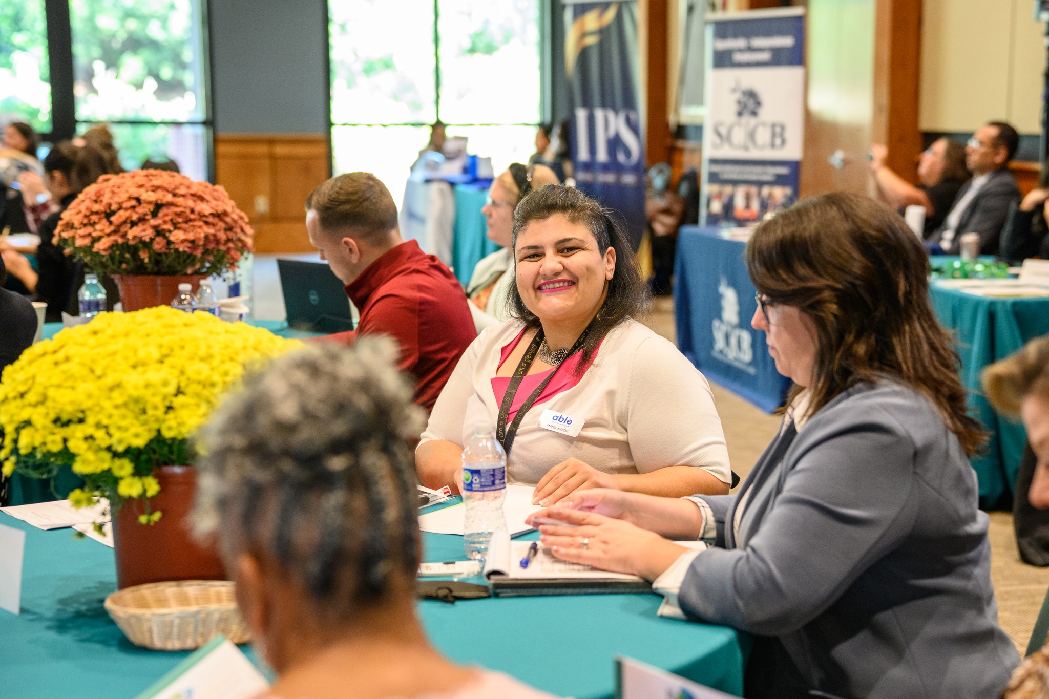 Photo of participants listening. Photo is focused on Able SC Director of Employment Programs, Marly, a Middle Eastern woman with dark hair using a wheelchair and smiling.