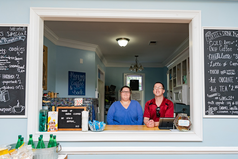 Two people working behind the counter at a coffee shop and smiling at the camera.